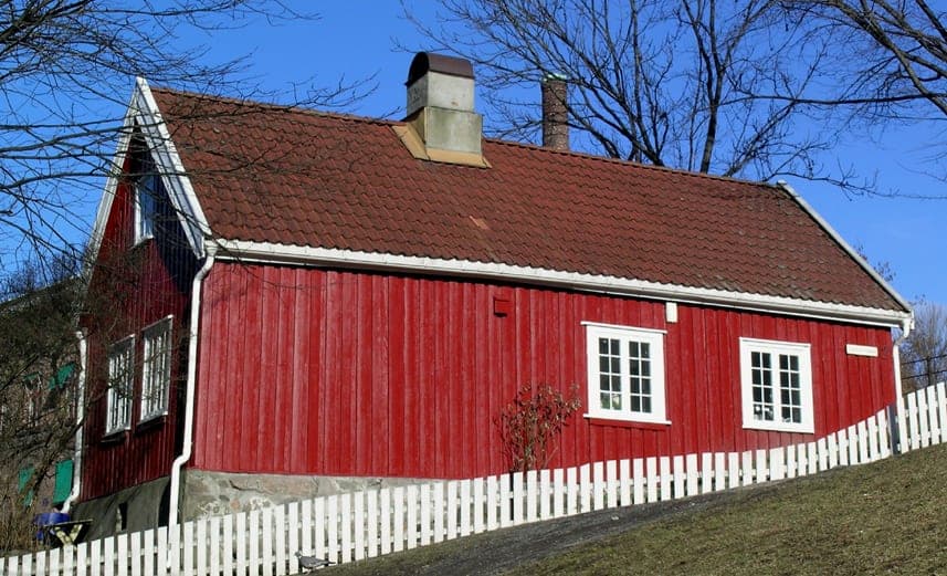 The red timber cottage behind its white picket fence
