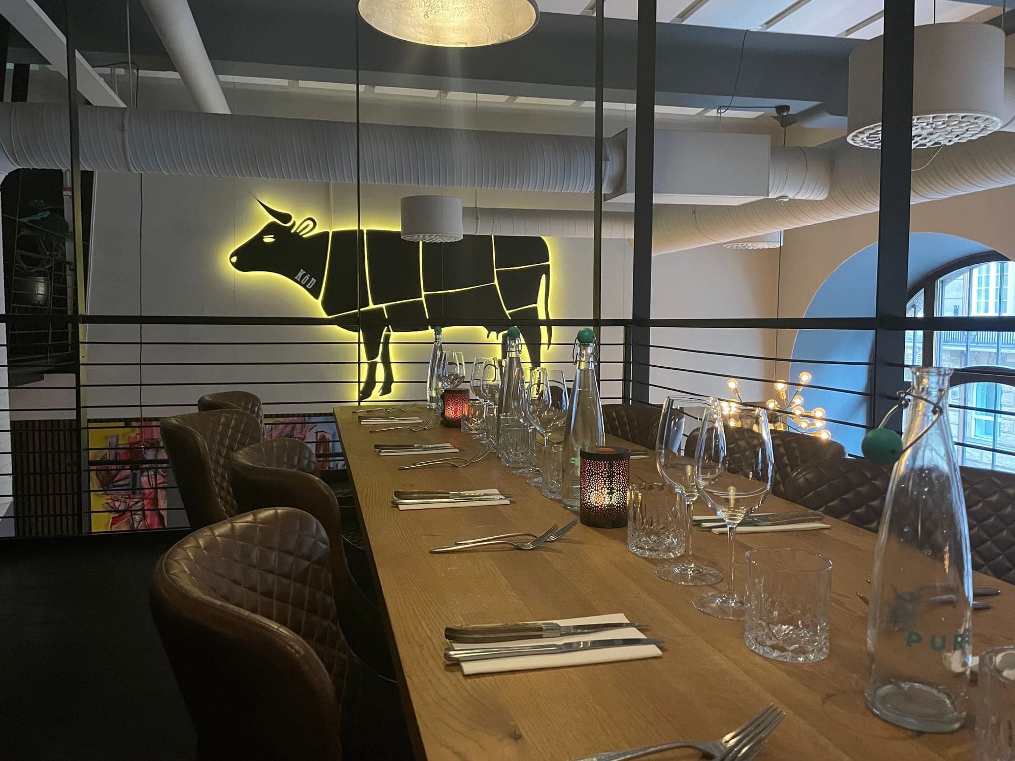 Long set table beneath KOD's neon butcher-cut cow sign