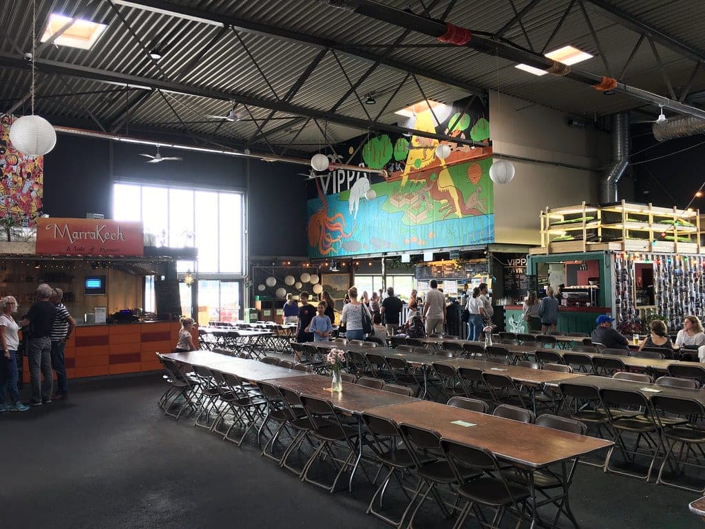 Interior of the Vippa street-food hall on the Oslo waterfront, with food stalls, communal tables and painted murals under an industrial roof.